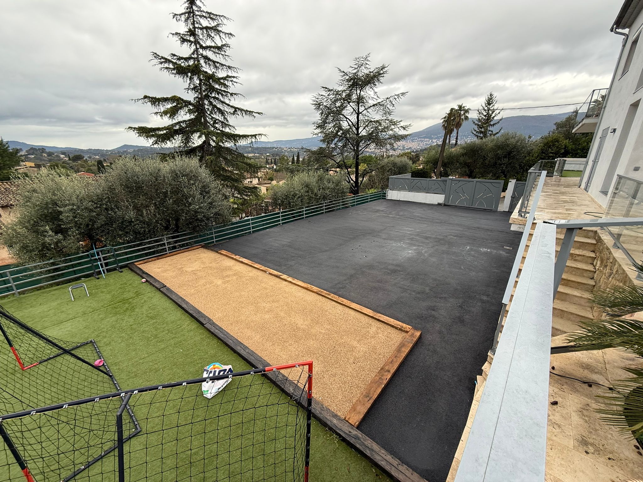 Cour de villa en enrobé noir avec terrain de pétanque et vue sur les collines