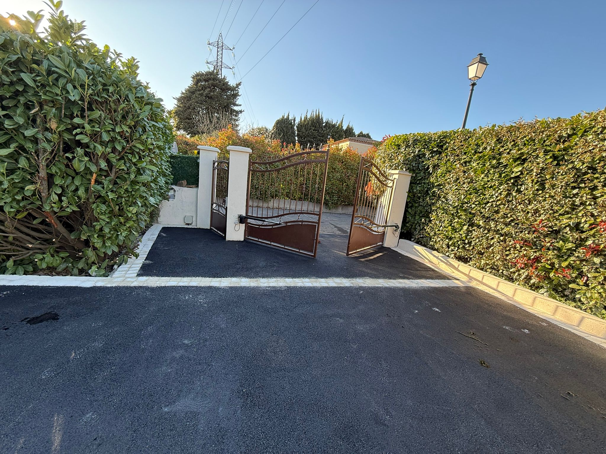 Entrée de villa avec portail fer forgé et accès en enrobé noir
